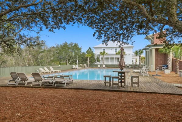 A swimming pool with lounge chairs and a deck area, surrounded by trees and a large house in the background. - Sandy Toes on Parks Edge (Orange Beach)