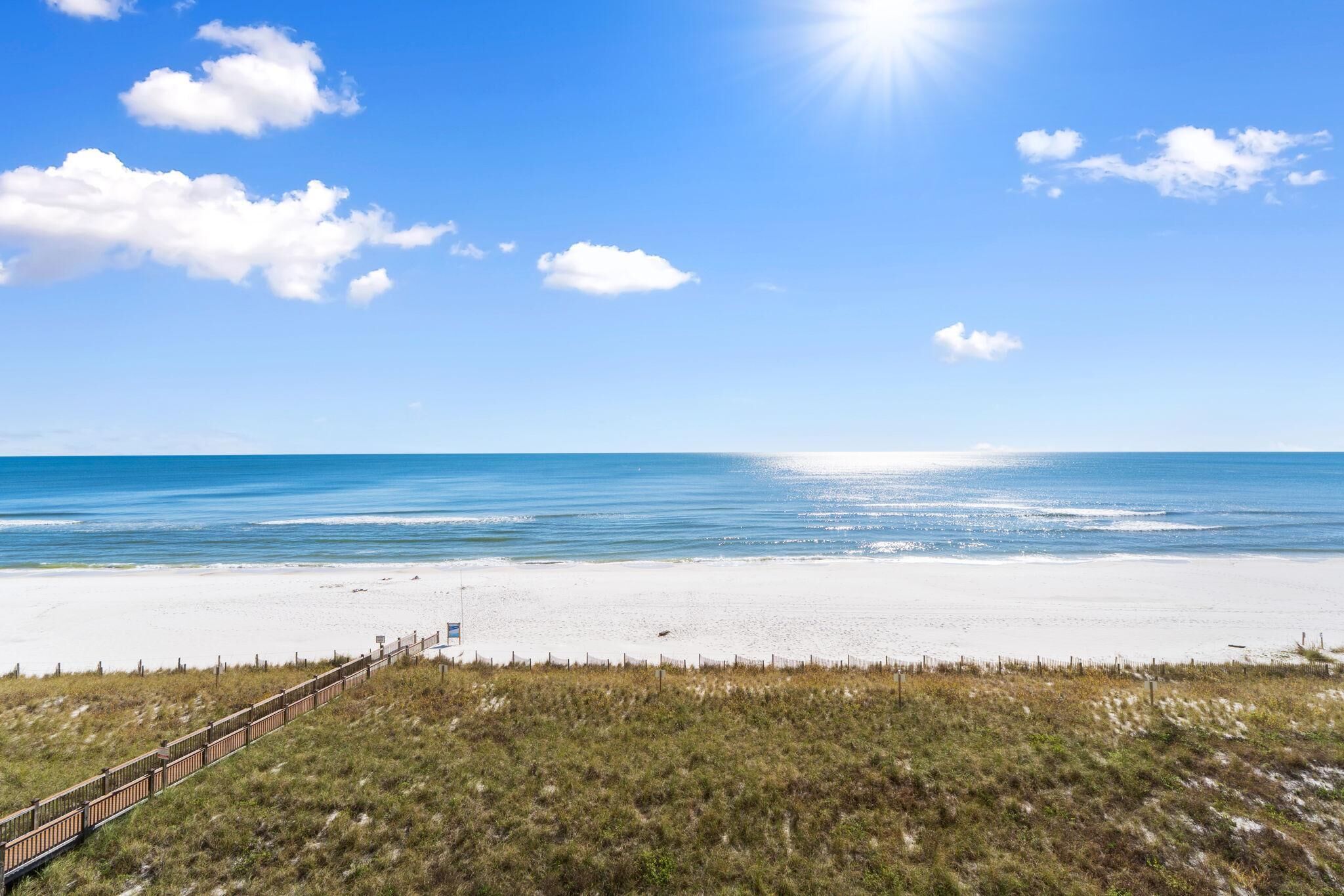A beach with a wooden boardwalk leading to the water, a clear sky, and a sandy shore.