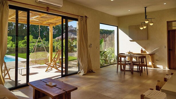 Amplia sala de estar con un gran ventanal corredizo que da a una piscina y jardín, una mesa de comedor de madera y un área de descanso confortable.