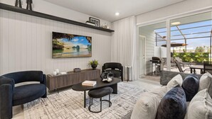 A modern living room with a large painting, a sofa, a coffee table, and a dining area with outdoor seating. - Last Minute Disney Getaway! Luxury Townhouse with Private Pool. Book Now! #148203 (Orlando)