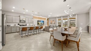 Een moderne keuken met witte kastjes, een centraal eiland met barstoelen, en een eetgedeelte met een grote houten tafel en stoelen.
