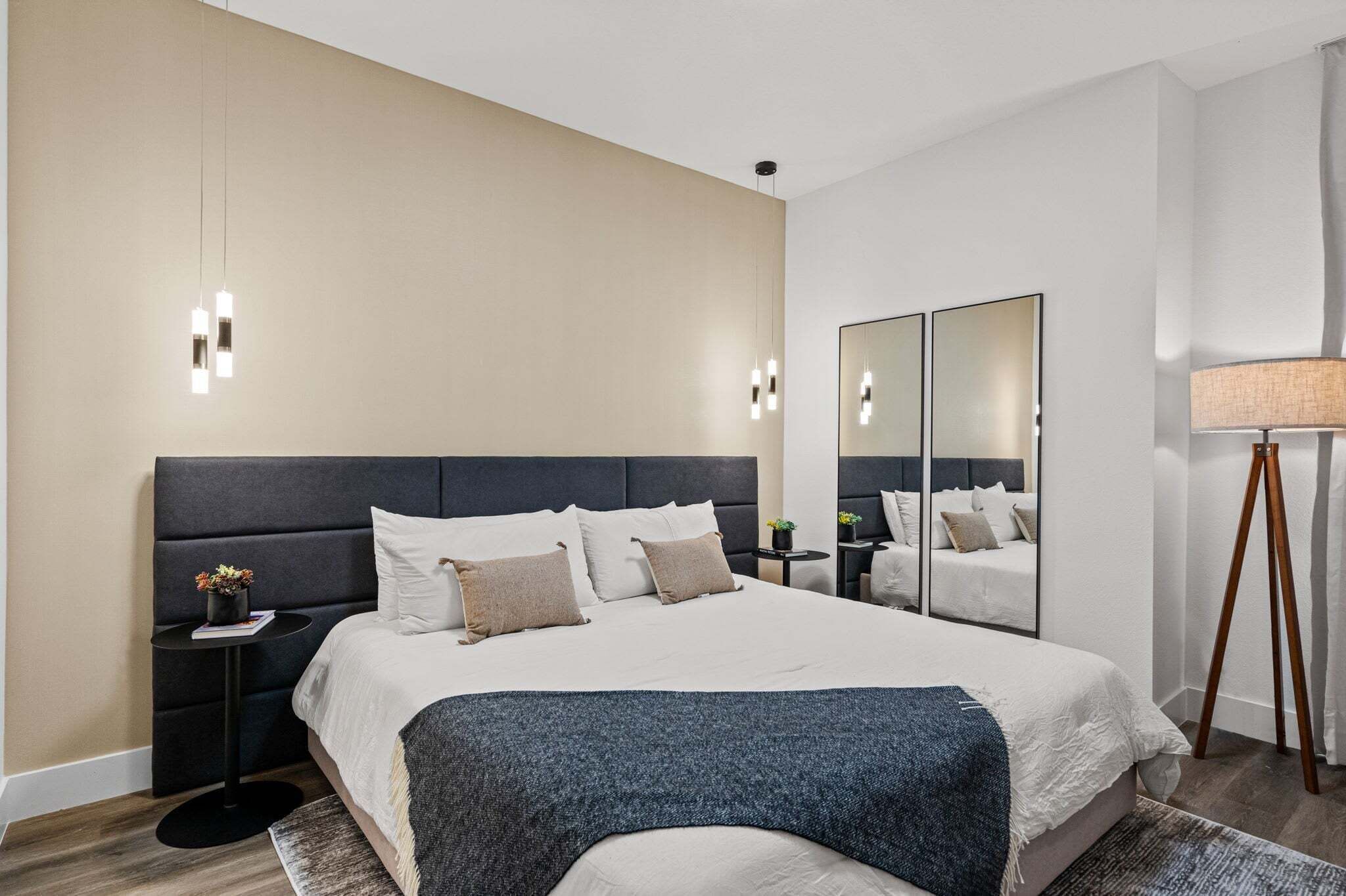 Una habitación de hotel moderna con una cama grande, mesitas de noche, un espejo y una lámpara.