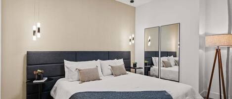 Una habitación de hotel moderna con una cama grande, mesitas de noche, un espejo y una lámpara.