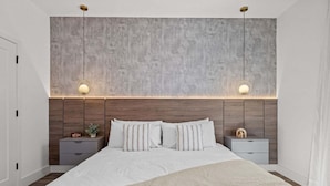 A modern bedroom with a large bed, two bedside tables, a nightstand, a wall clock, and a textured headboard. - Disney! Luxury Townhouse with Private Pool & Themed Bedrooms. Book Now! #DP67 (Orlando)