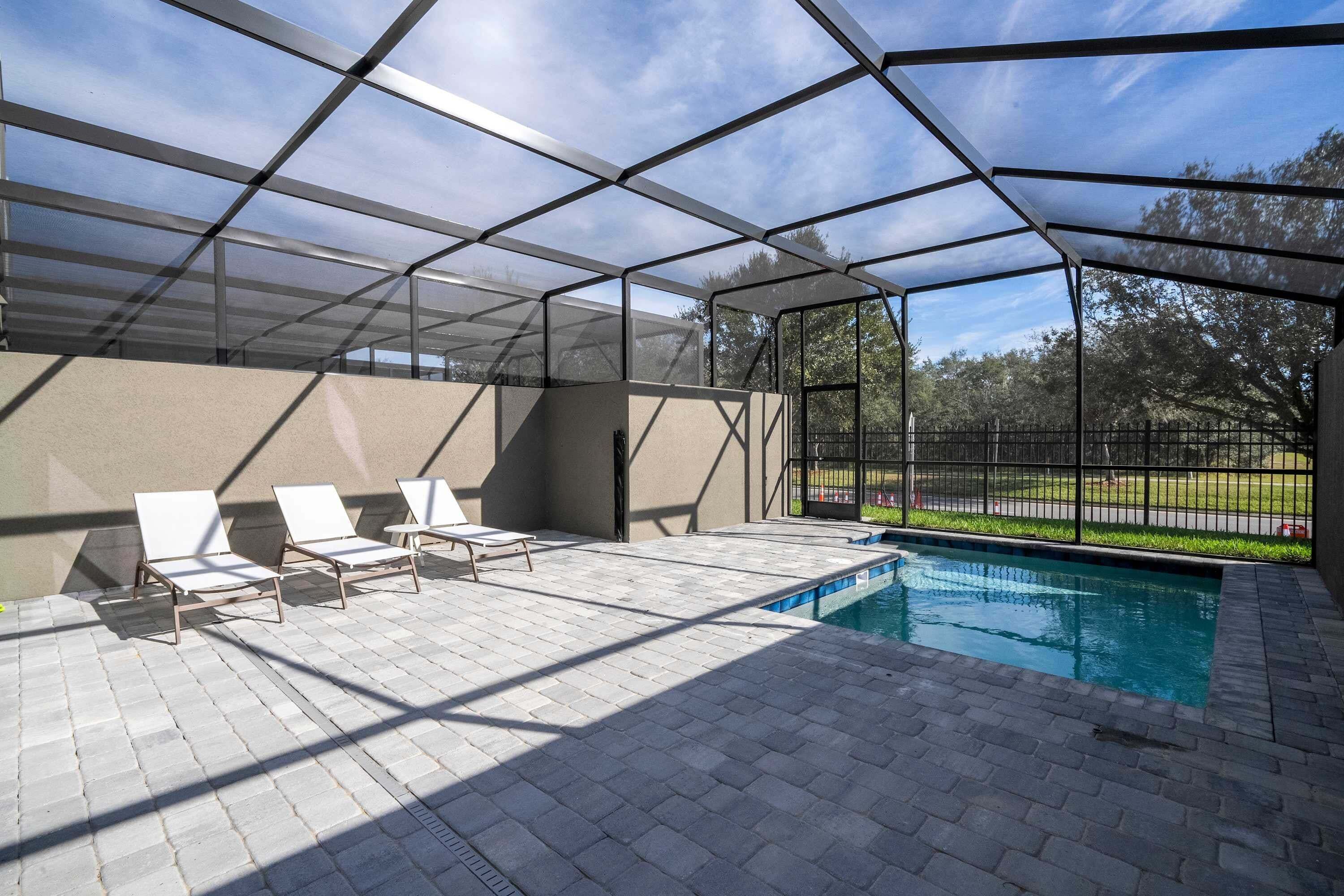 A covered outdoor area with a pool, lounge chairs, and a view of the surrounding landscape.