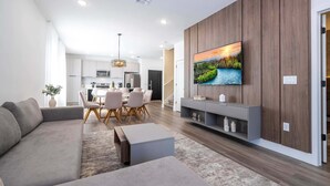 A modern living room with a sofa, coffee table, and TV wall mounted above a wooden panel wall. - Disney! Luxury Townhouse with Private Pool & Themed Bedrooms. Book Now! #DP71 (Orlando)