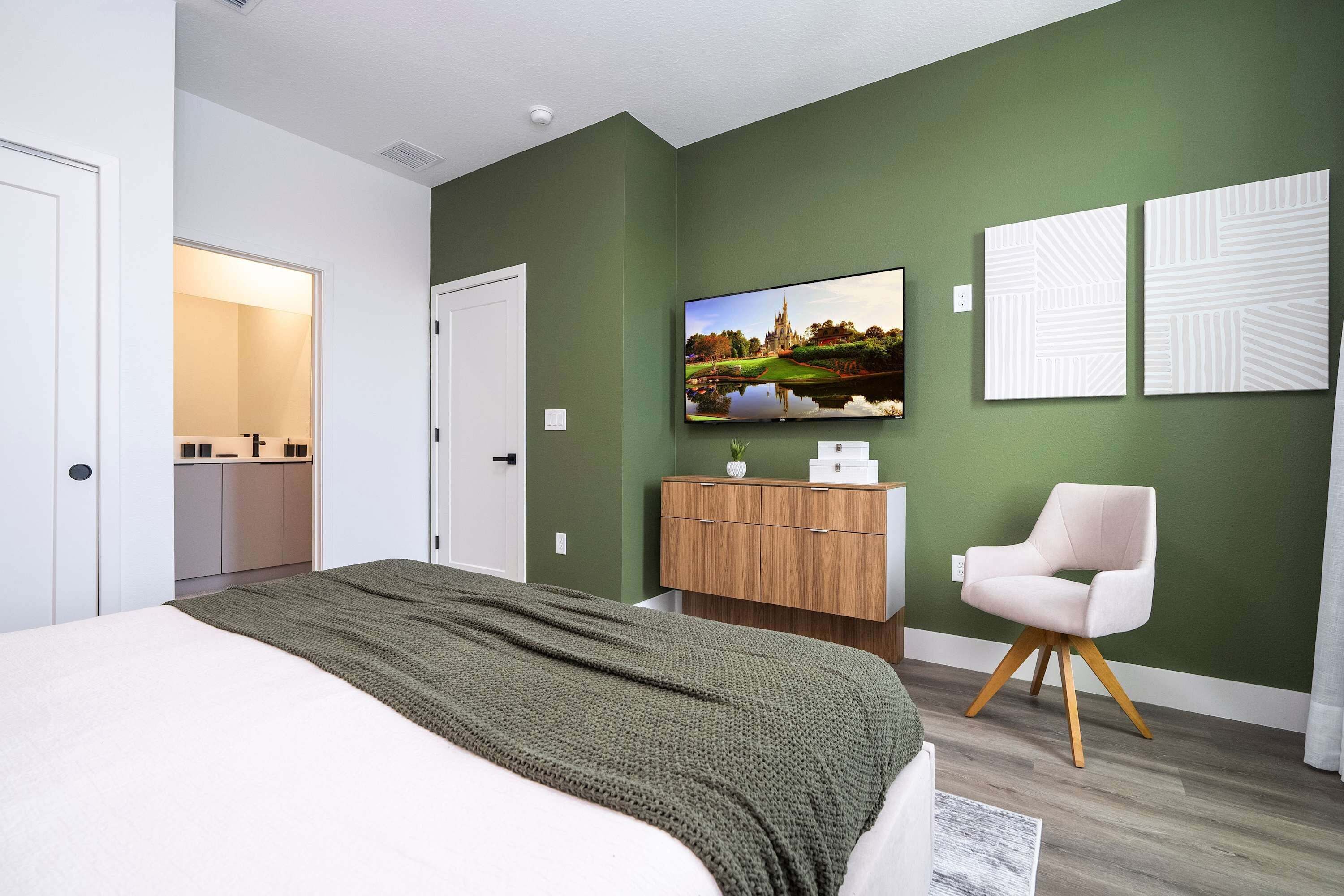 Ein modernes Schlafzimmer mit Bett, Schminktisch, Fernseher und Stuhl.