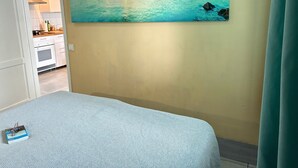 Un dormitorio con una cama, un cuadro de una escena costera y vistas a una cocina.