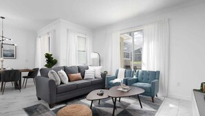 Ein modernes Wohnzimmer mit einem grauen Sofa, blauen Sessel, einem Couchtisch und einem Essbereich mit Tisch und Stühlen.