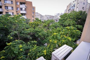 Ein mehrstöckiges Wohngebäude mit Balkonen und ein dichter Baum mit gelben Blüten im Vordergrund.