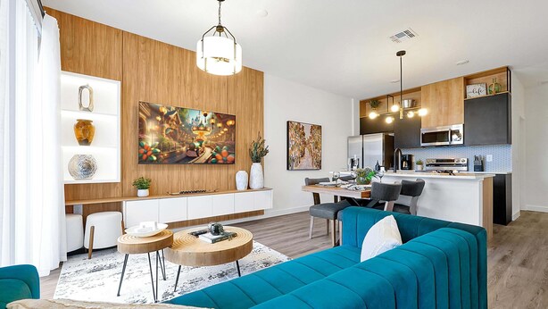 Uma sala moderna com sofá verde-água, detalhes em madeira e uma área de jantar com cozinha ao fundo.