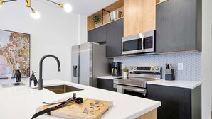 Cozinha moderna com ilha central, eletrodomésticos de aço inoxidável e diversos armários.