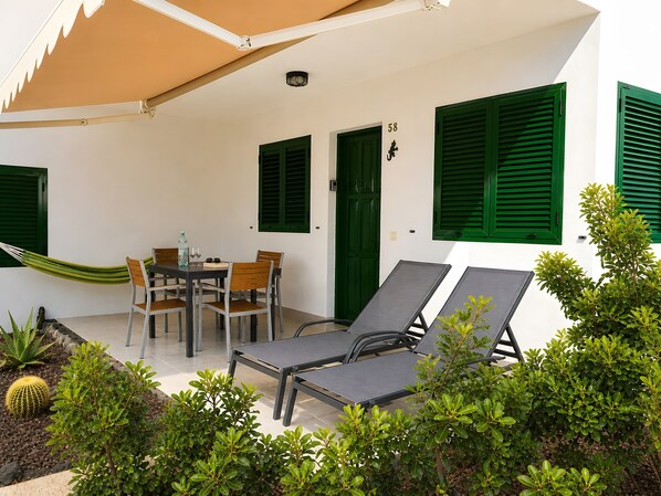 Eine überdachte Terrasse mit Tisch und Stühlen, zwei Liegestühlen und einer Hängematte.