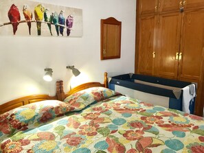 Ein Schlafzimmer mit blumigem Bettbezug, einem Holzschrank und einem Wandbild mit Vögeln.