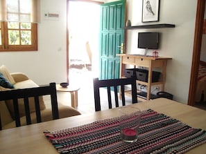 Ein Essbereich mit Tisch, Stühlen, einer gewebten Tischmatte, einer Kerze und einem Fernseher auf einem Regal.