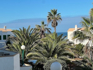 A coastal building with palm trees, a lamp post, and a view of the sea.