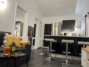 A modern kitchen with a built-in oven, a refrigerator, and a microwave. There are three bar stools and a dining table. - Apartment 'La Barca Sunny Rooftop' with Sea View, Shared Terrace & Wi-Fi (El Cotillo)