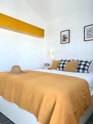 Ein ordentlich bezogenes Bett mit einer braunen Decke, einem karierten Kopfkissen und einem Hut auf dem Bett.