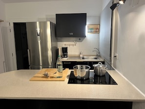 A kitchen with a stainless steel refrigerator, a coffee maker, a sink, and a countertop with a cutting board and pots. - Apartment 'La Barca Sunny Rooftop' with Sea View, Shared Terrace & Wi-Fi (El Cotillo)
