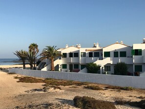Um edifício costeiro com várias varandas, paredes brancas e persianas verdes.