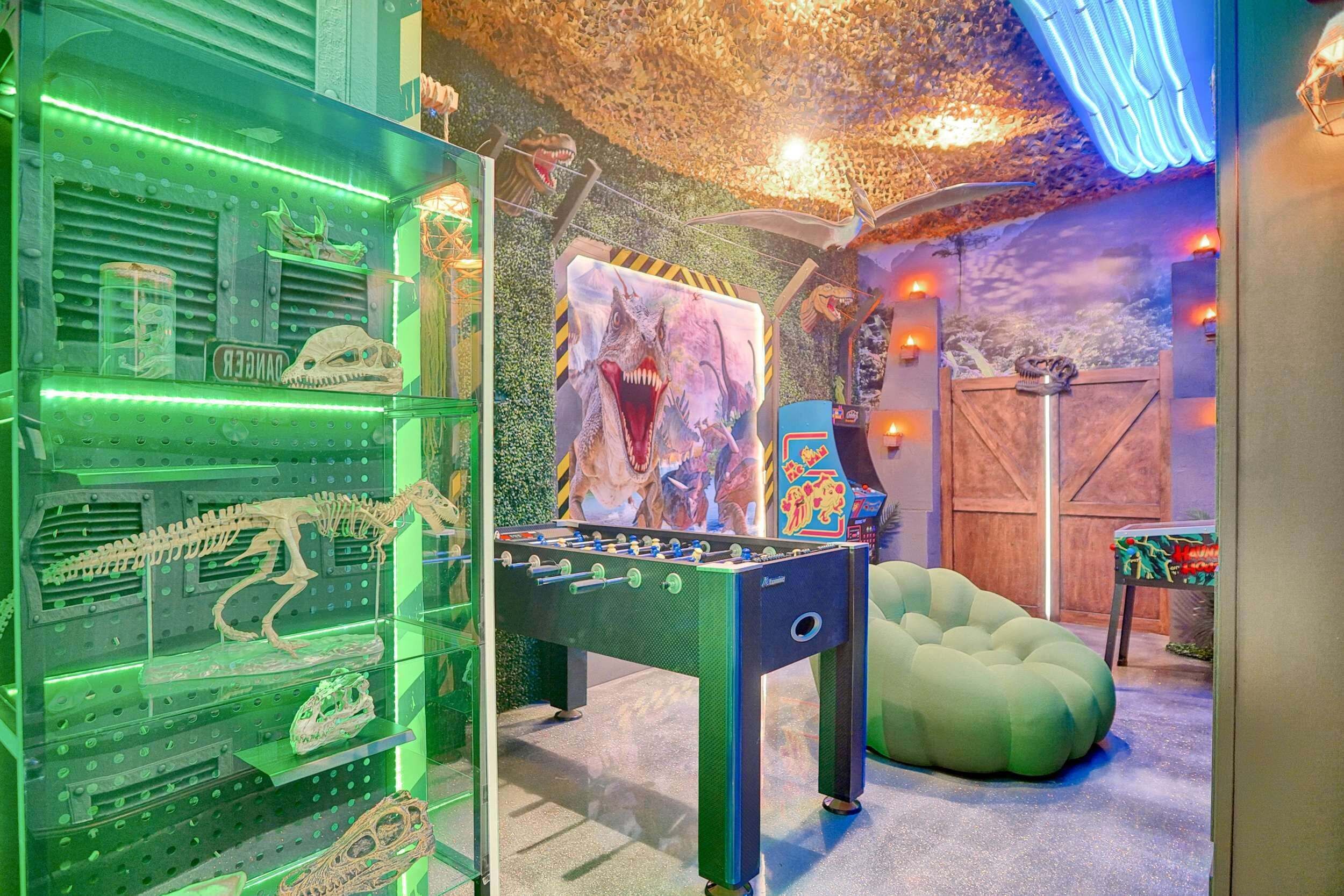 A room with a foosball table, dinosaur skeletons, and a large painting of a dinosaur.