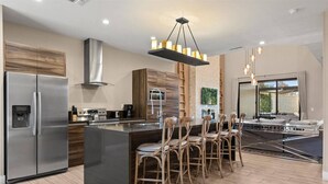 A modern kitchen with a stainless steel refrigerator, a central island with bar stools, and a dining area with a view. - Last Minute Disney Getaway! Private Terrace & Comfortable Bedrooms. Book Now! #159485 (Orlando)