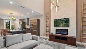 A modern living room with a sofa, ottoman, TV, and fireplace. - Last Minute Disney Getaway! Private Terrace & Comfortable Bedrooms. Book Now! #159485 (Orlando)