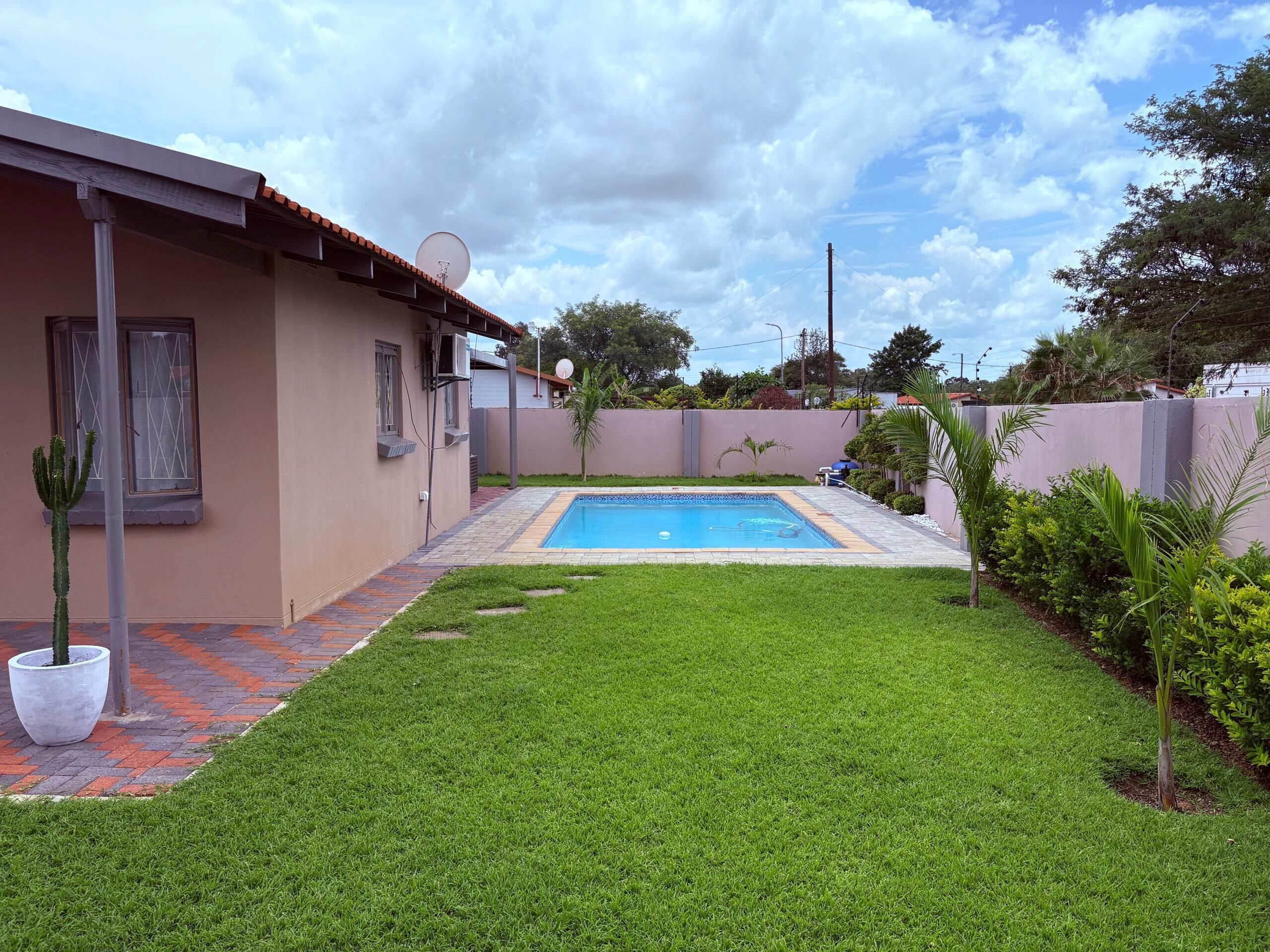 Un patio trasero residencial con piscina, césped cuidado y una antena parabólica en la casa.