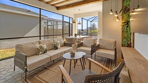 A modern outdoor living area with a sofa set, a round table, and wicker chairs. - Last Minute Disney Getaway! Luxury Villa with Private Pool, Game Room & Themed Bedrooms. Book Now! #151423 (Orlando)