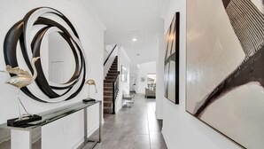 Un couloir moderne agrémenté d’une console en verre, d’un grand miroir rond et d’œuvres d’art murales abstraites.