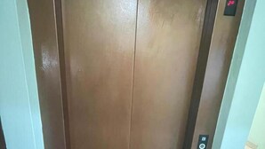 An elevator with a brown door, a control panel with a button, and a small sign above it.