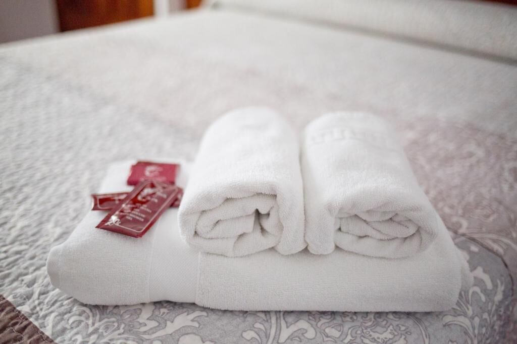 Une serviette blanche, soigneusement pliée, avec une étiquette rouge, posée sur un couvre-lit à motifs.