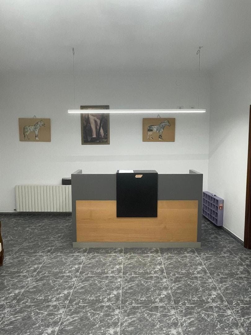 A reception desk with a wooden counter and a black towel hanging on it. There are three framed artworks on the wall above the desk. The floor is tiled with a marble pattern.