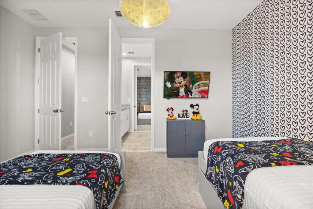 Ein Schlafzimmer mit zwei Betten, einem Fernseher an der Wand und einem Mickey Mouse Poster.