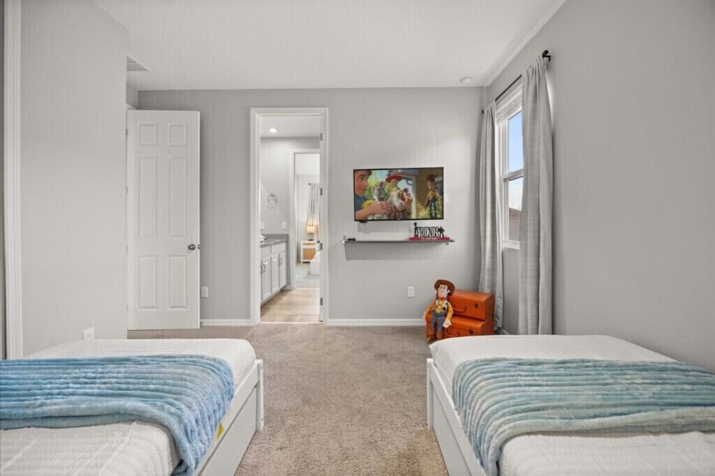Un dormitorio con dos camas, un televisor montado en la pared y una puerta que da a otra habitación.