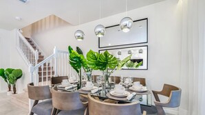 Et moderne spiseområde med trappe, spisebord dækket til fire personer og store, grønne planter.