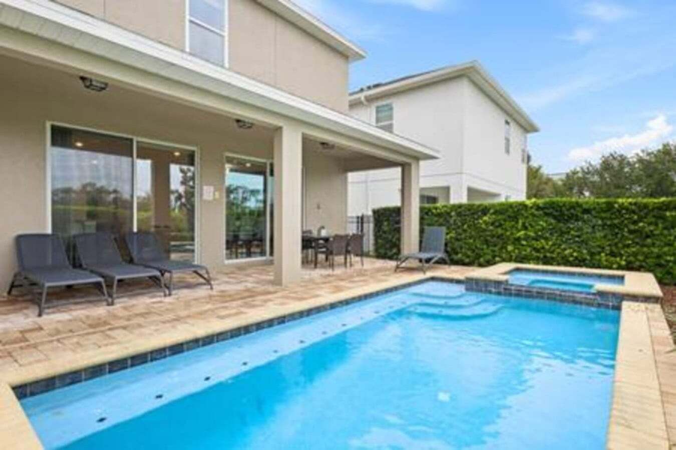 A swimming pool with lounge chairs, a covered patio, and a hedge.
