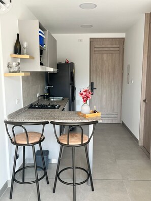 Eine kompakte Küche mit einer zentralen Kochinsel, zwei Barhocker, einem Kühlschrank und einer Holztür.