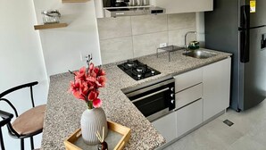 A modern kitchen with a granite countertop, built-in oven, and a black refrigerator. There is a small dining area with a chair and a vase of flowers on the counter. - Cozy 1-bedroom apartment in charming Urb Don Jaca with AC (Urb Don Jaca)