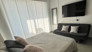 A modern bedroom with a large bed, a sofa, a TV, and a window with blinds. - Cozy 1-bedroom apartment in charming Urb Don Jaca with AC (Urb Don Jaca)