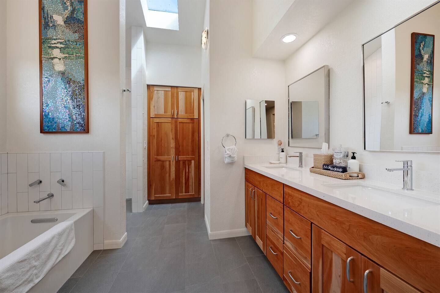A modern bathroom with a freestanding bathtub, wooden vanity, and large mirrors.