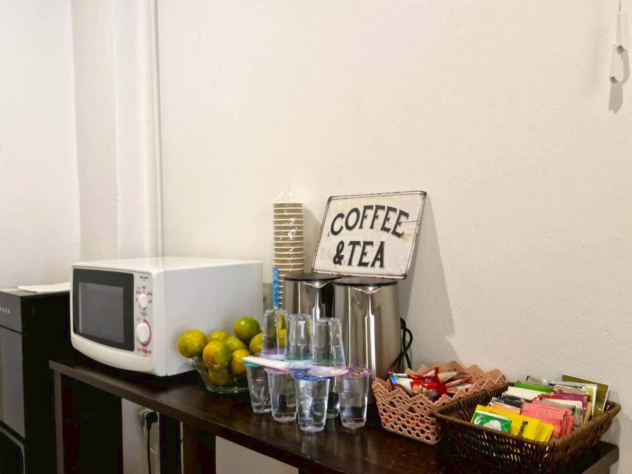 A kitchen counter with a microwave, a sign reading "Coffee & Tea", a basket of magazines, and a glass of water.