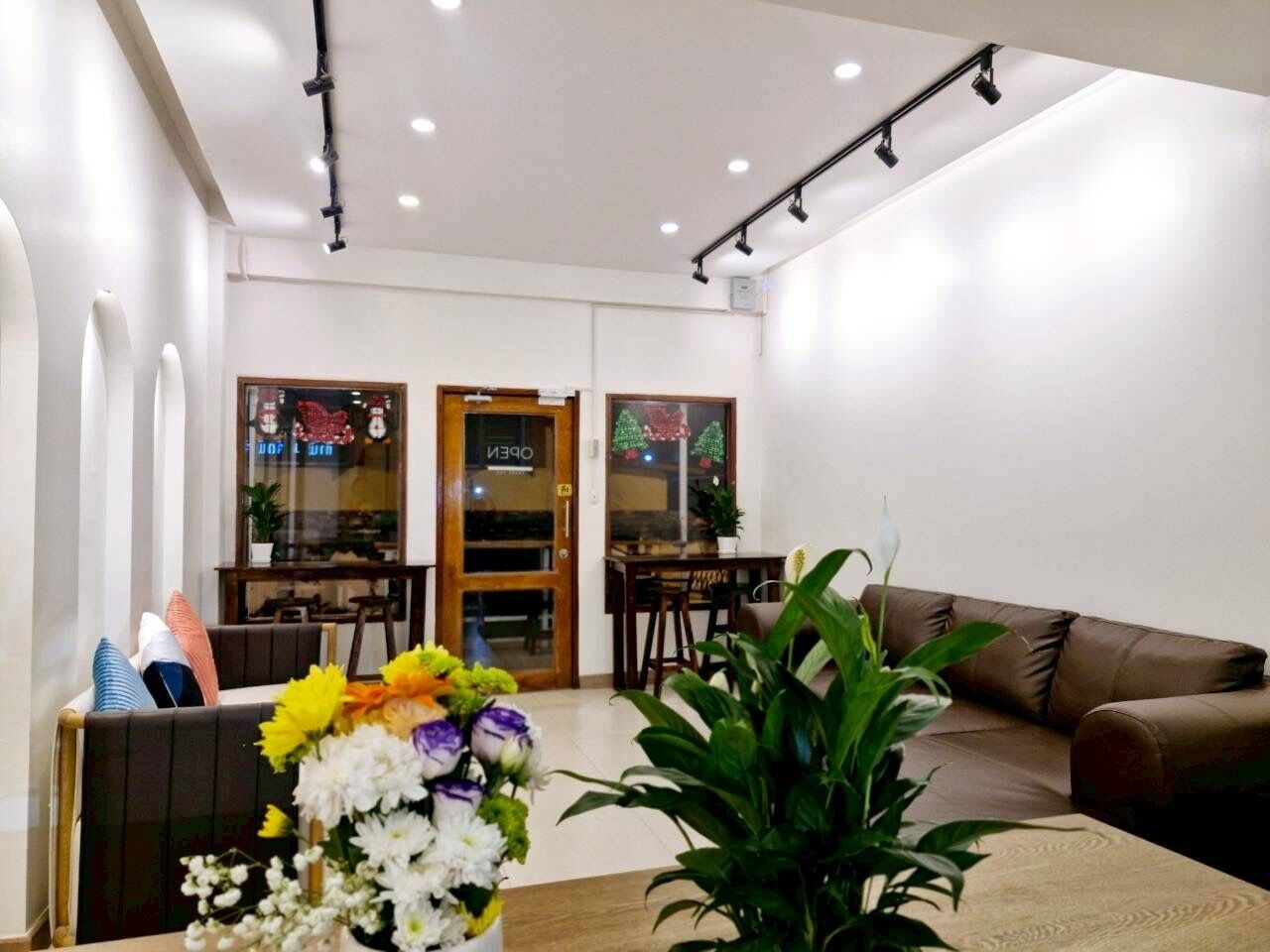 Una sala moderna con un sofá de cuero marrón, una mesa de centro de madera y un arreglo floral. Se ve un área de comedor con una mesa y sillas de madera al fondo.