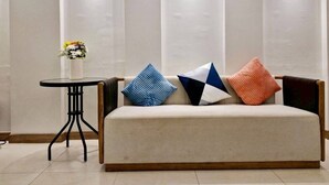 A modern living room with a beige sofa, three pillows, a small round table with a vase of flowers, and three wall-mounted light fixtures. - MaMa Hostel  CNX (Chiang Mai)