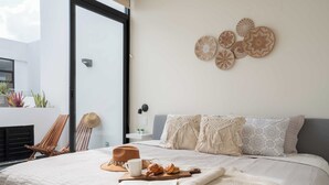 Ein Schlafzimmer mit einem Bett, einem Buch, einer Tasse und einem Hut auf dem Bett. Zwei Stühle und ein Tisch mit Hut und Tasse darauf.