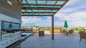 An outdoor patio with a built-in grill, seating area, and a view of the landscape. - Beach Way Carneiros #209 - Quadruple by Carpediem (Tamandaré)