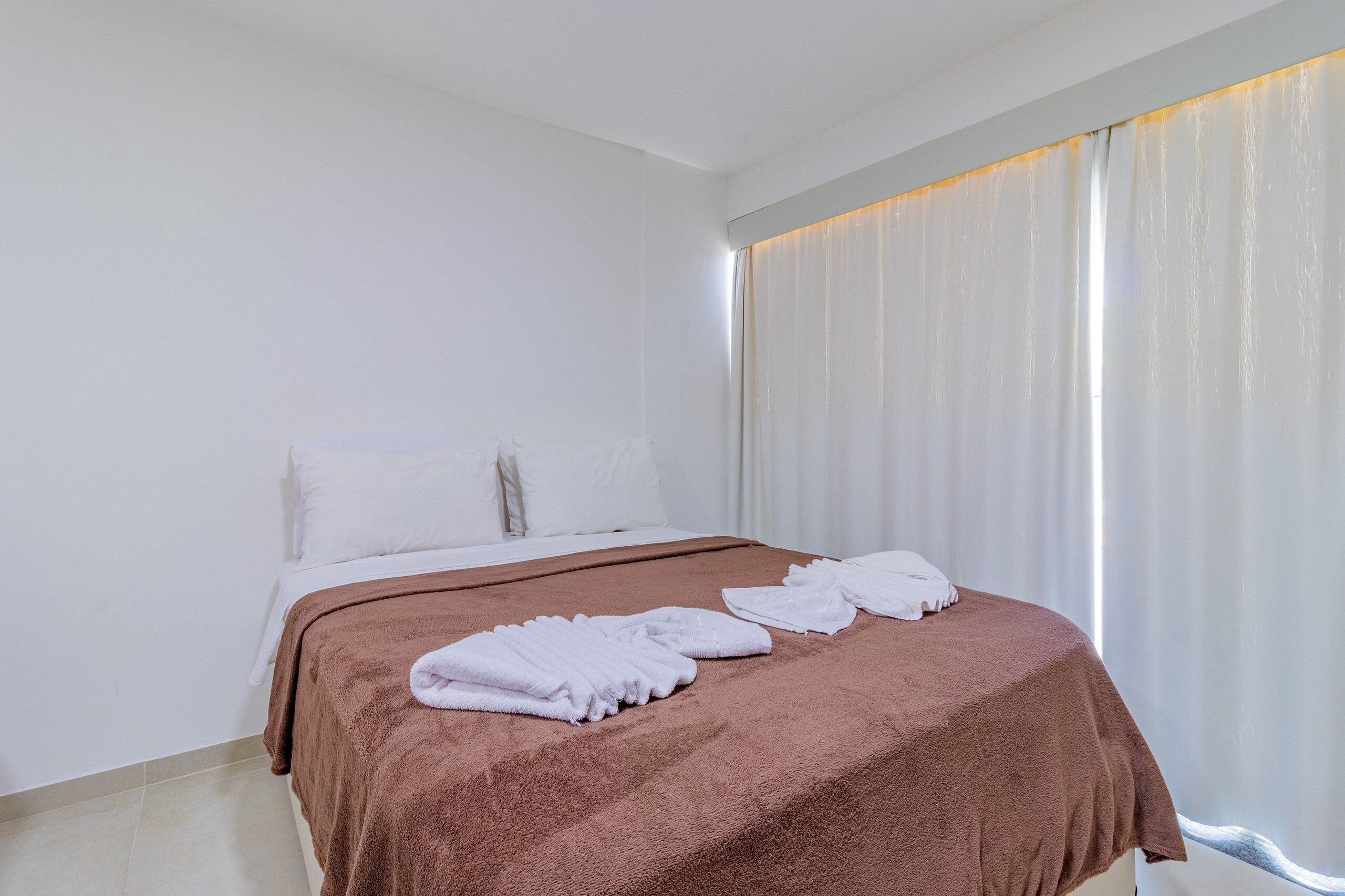 Una habitación de hotel con una cama, cortinas blancas y una manta marrón.