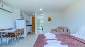 A hotel room with a bed, a dining table with chairs, a kitchenette, and a sofa. - Beach Way Carneiros #209 - Quadruple by Carpediem (Tamandaré)