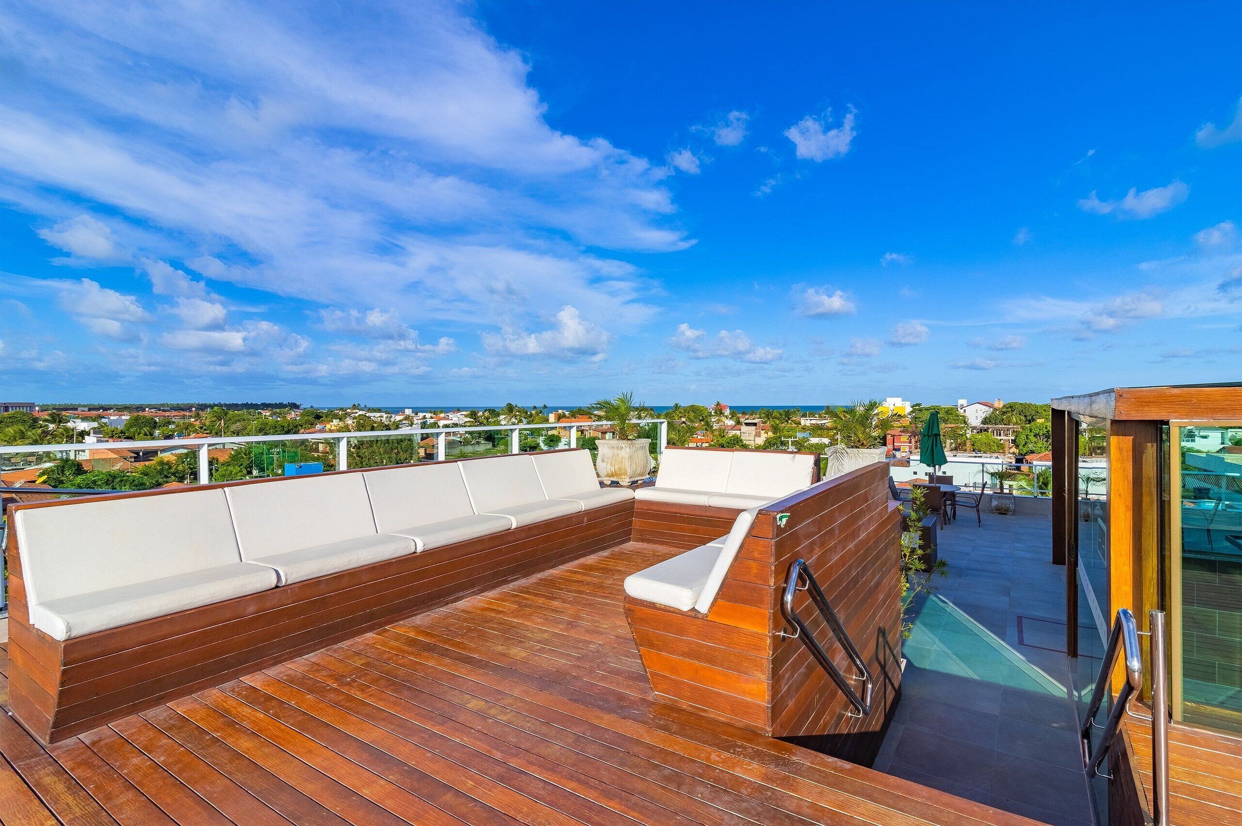 Una terraza de madera con un banco integrado, una puerta de cristal que da a un área cubierta y vistas de la ciudad.