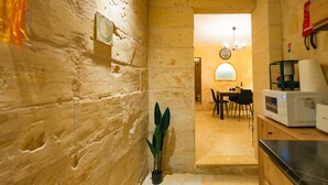 A narrow stone-walled kitchen with a dining area in the background, a potted plant, and a microwave on the counter. - Comfy 2 BR Flat in the Heart of Floriana (Floriana)